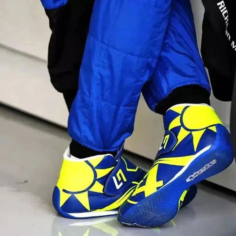 Blue and yellow Lando Norris 2023 F1 Racing shoes with sun design worn by a person in blue pants.