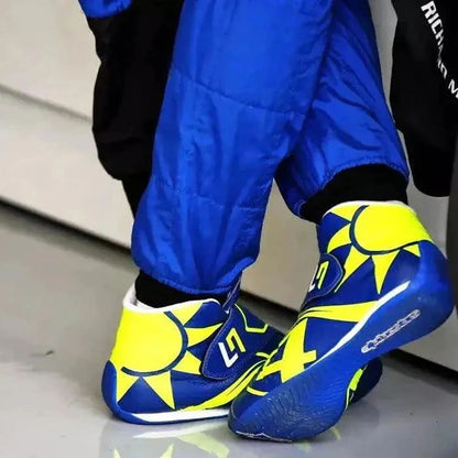 Blue and yellow Lando Norris 2023 F1 Racing shoes with sun design worn by a person in blue pants.