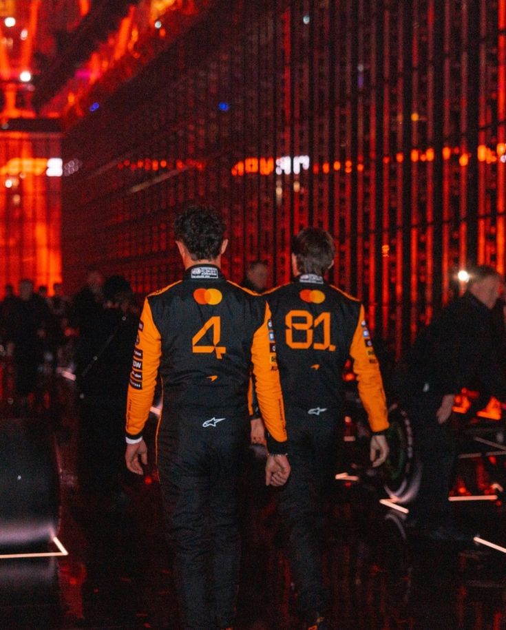 Back View of Lando Norris and Oscar Piastri in a 2025 McLaren orange F1 racing suit with '4' and '81' branding.
