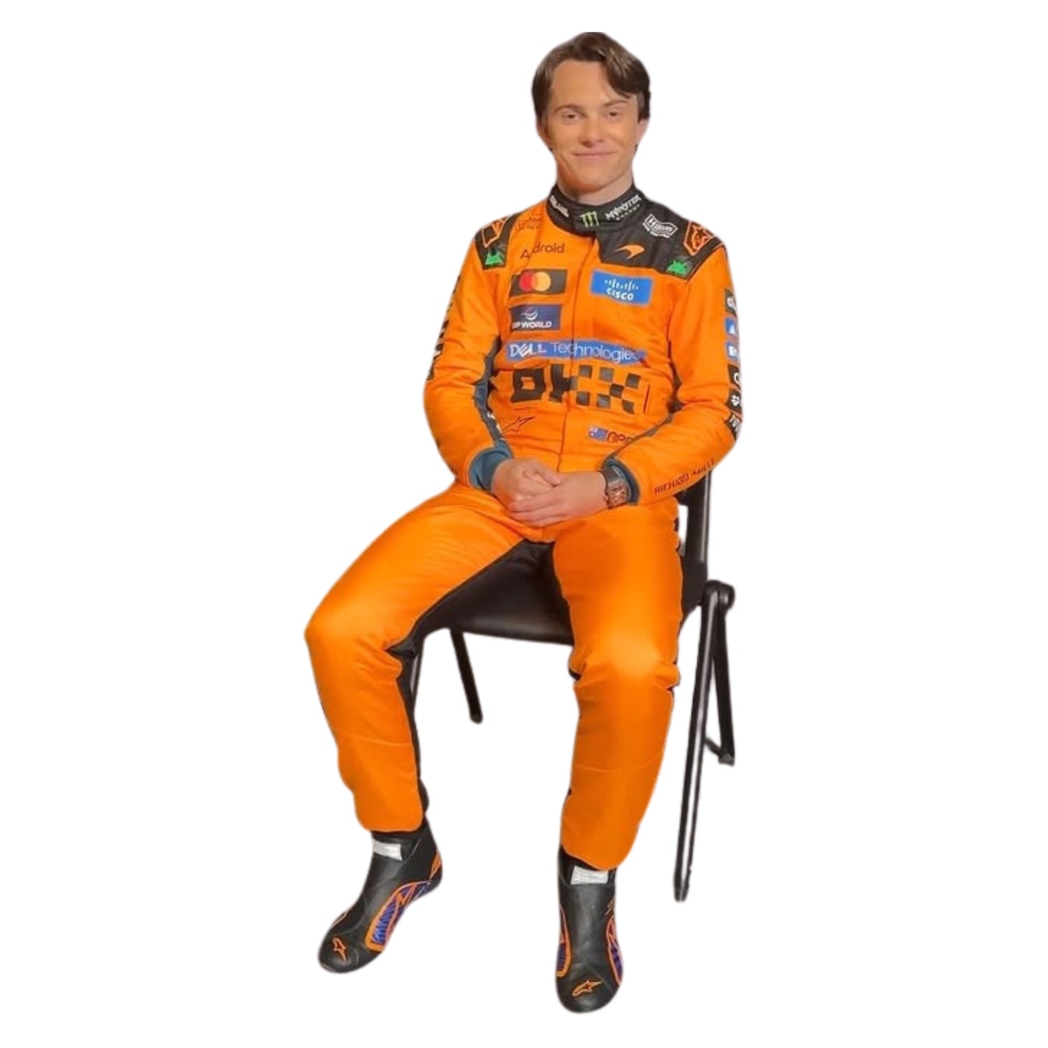 Oscar Piastri wearing an orange 2026 racing suit sitting on a chair with a white background